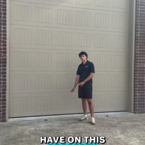 Man in a dark polo pointing at a tan garage door on a brick home